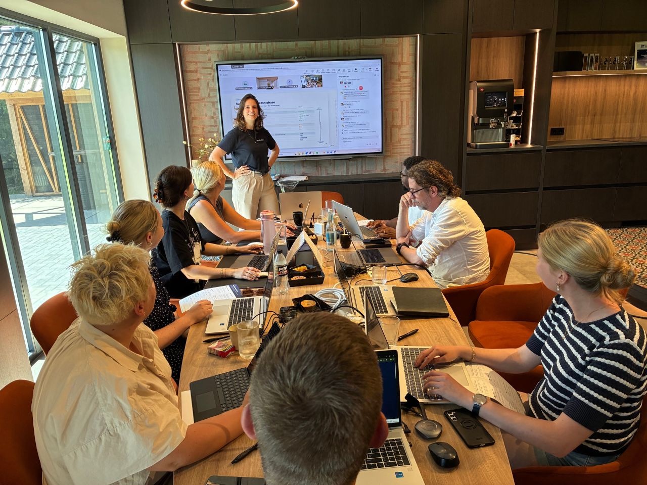 Carolina training a team around a table while participants work on their laptops